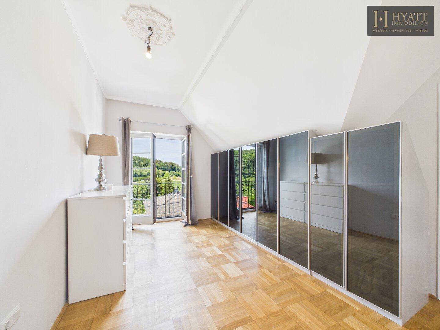 Schlafzimmer mit Parkettboden, Spiegelschränken und französischem Balkon mit Aussicht.