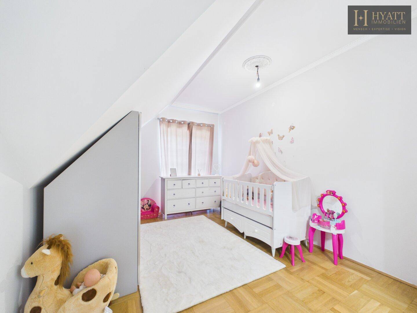 Helles Kinderzimmer mit Parkettboden, Babybett und Dachschräge.