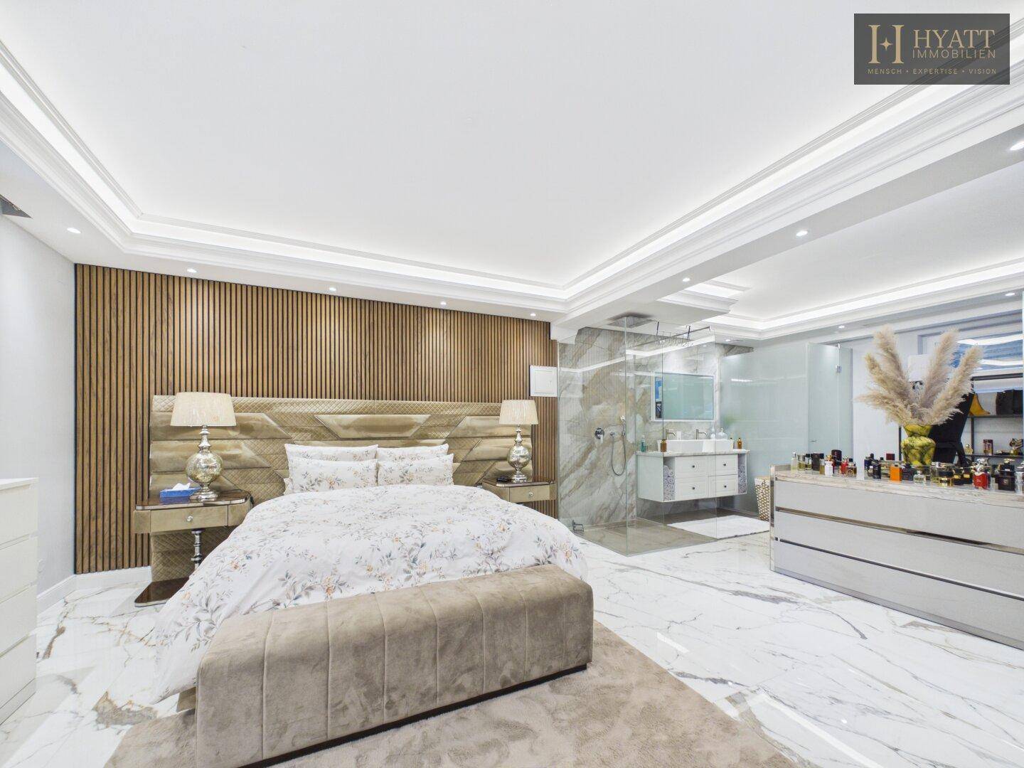 Luxuriöses Schlafzimmer mit offenem Badbereich, Marmorboden und stilvoller Holzvertäfelung an der Wand.