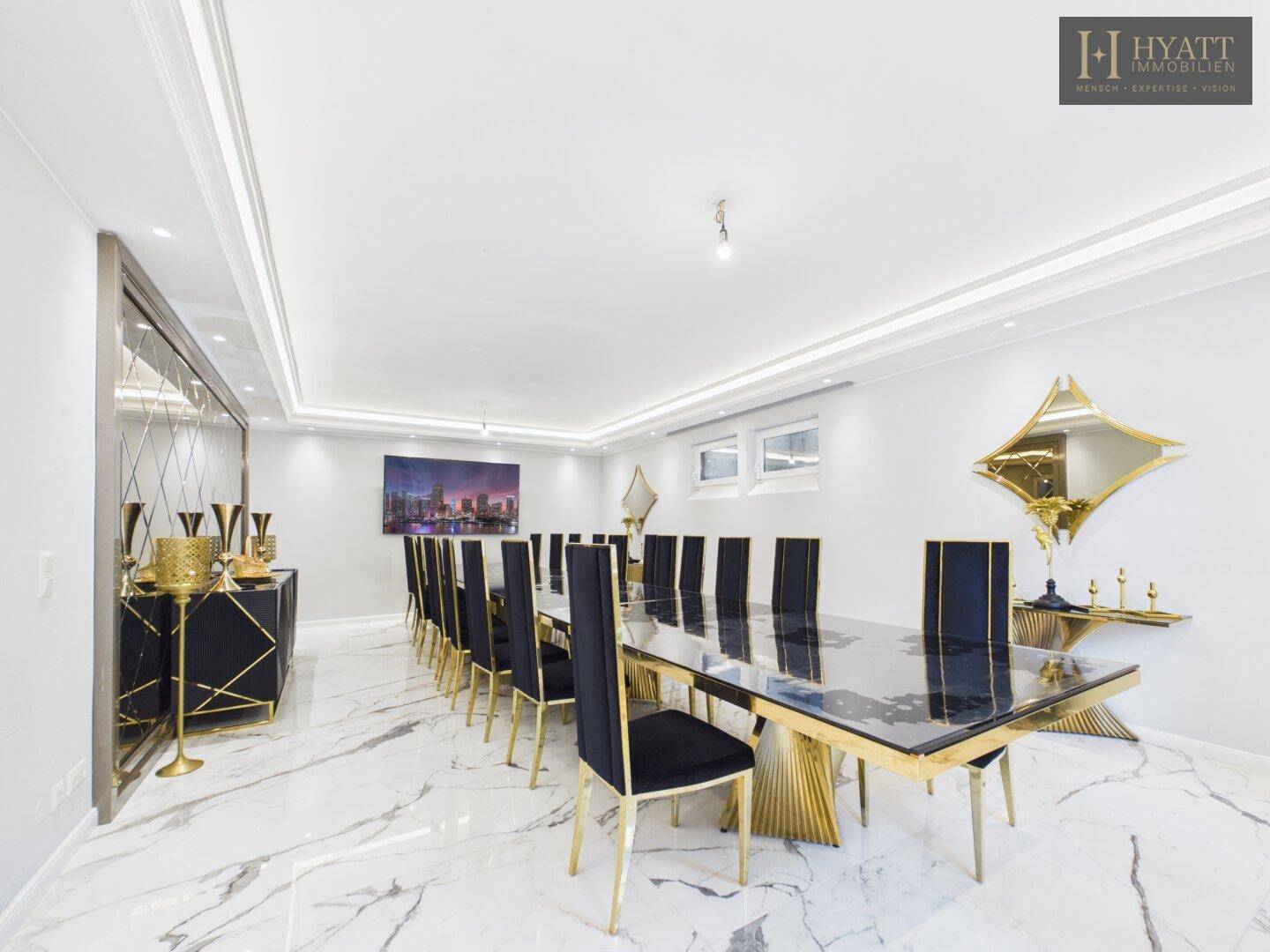 Großer, luxuriöser Essbereich mit langem schwarzen Tisch, goldenen Stühlen und Marmorboden.