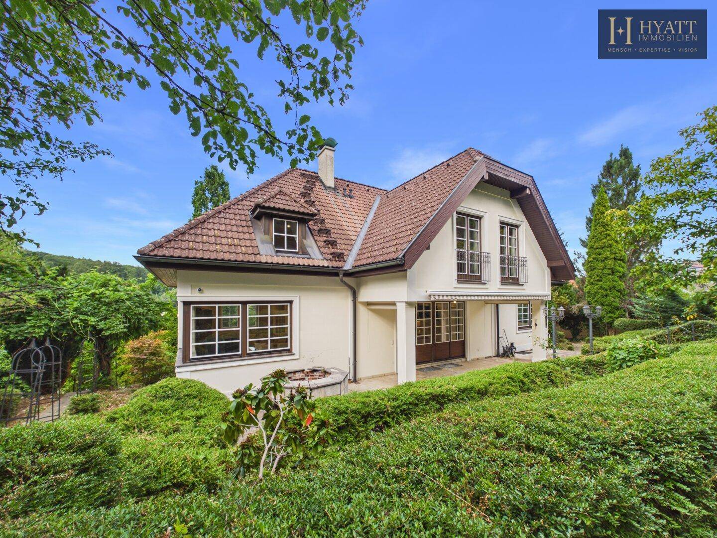Seitliche Ansicht des Hauses mit weitläufigem Garten, üppiger Vegetation und altem Baumbestand.