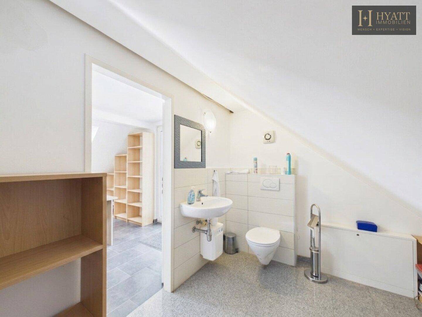 Dachgeschoss-Badezimmer mit WC, Waschbecken und Spiegel unter einer schrägen Decke.