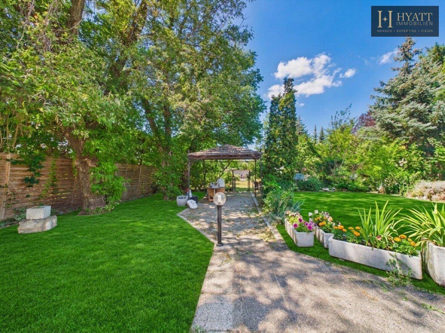 Gepflegter Garten mit Rasenfläche, gepflastertem Weg, Blumenbeeten und einem Pavillon.