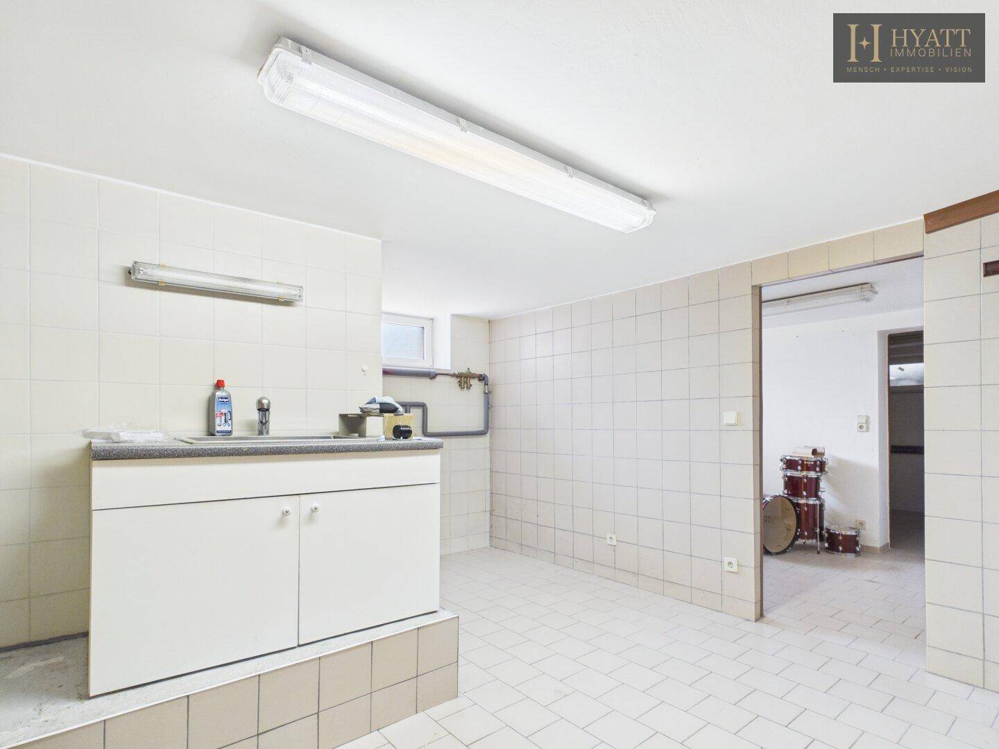 Gefliester Hauswirtschaftsraum mit Waschbecken, Arbeitsplatte und Stauraum im Keller.
