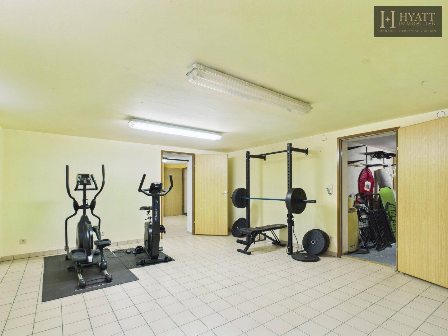 Fitnessraum im Keller mit verschiedenen Trainingsgeräten und Fliesenboden.