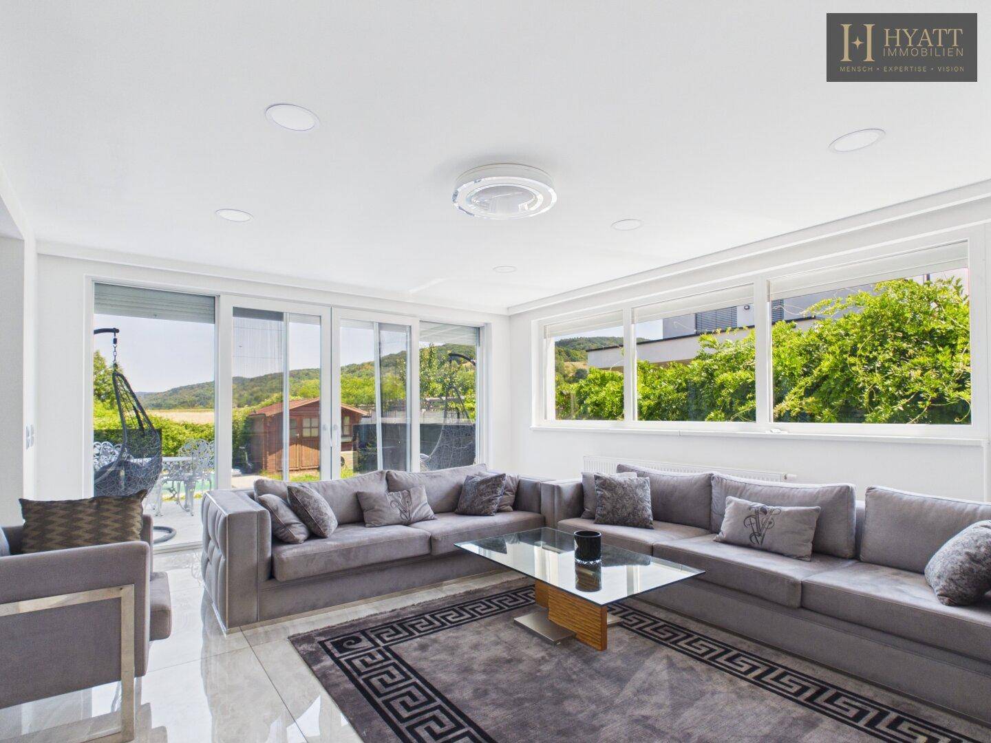 Helles Wohnzimmer mit großem Ecksofa, Fliesenboden und Zugang zur Terrasse mit Gartenblick.