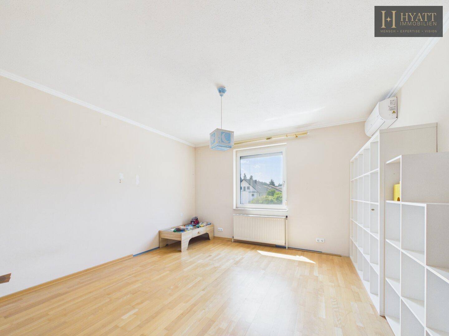 Helles Schlafzimmer mit Holzboden, weißem Regal und Fenster mit Blick auf die Umgebung.
