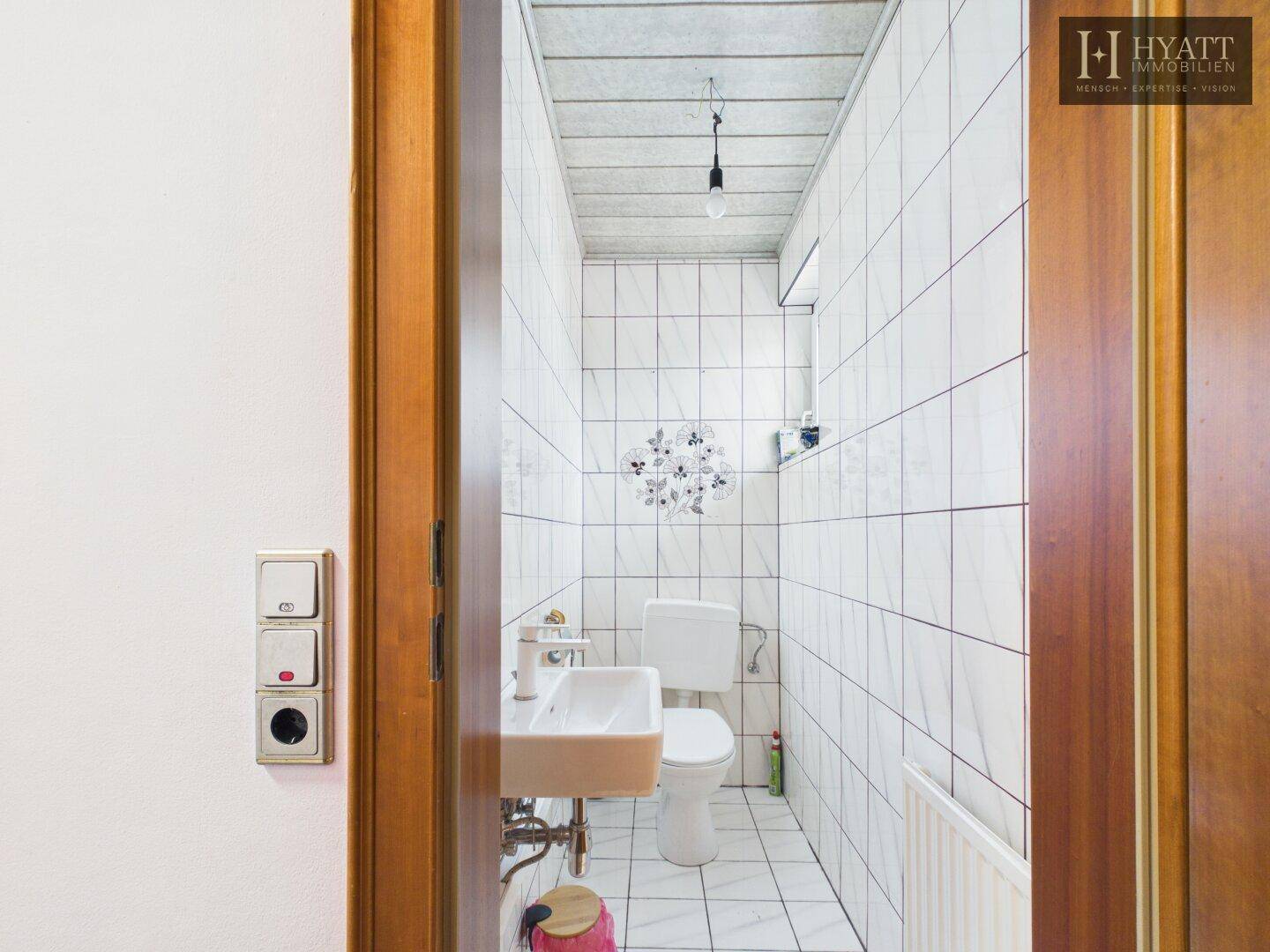 Kleines Gäste-WC mit weißen Fliesen, Waschbecken und Toilette.