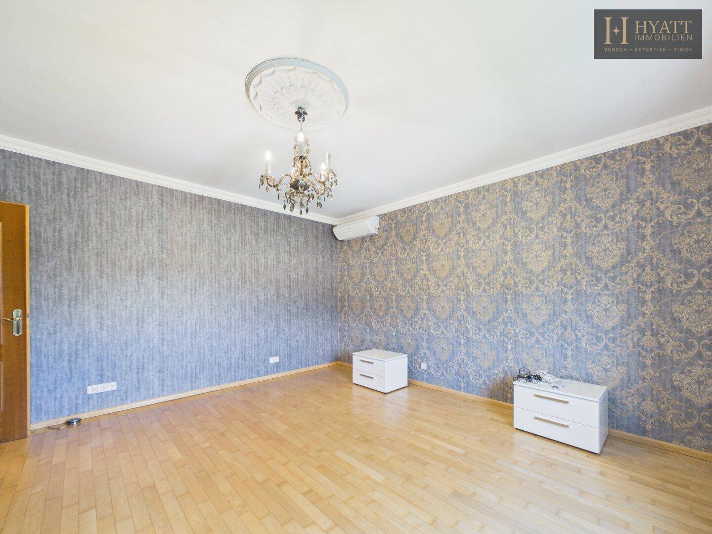 Geräumiges Schlafzimmer mit gemusterter Tapete, Holzboden und Kronleuchter.