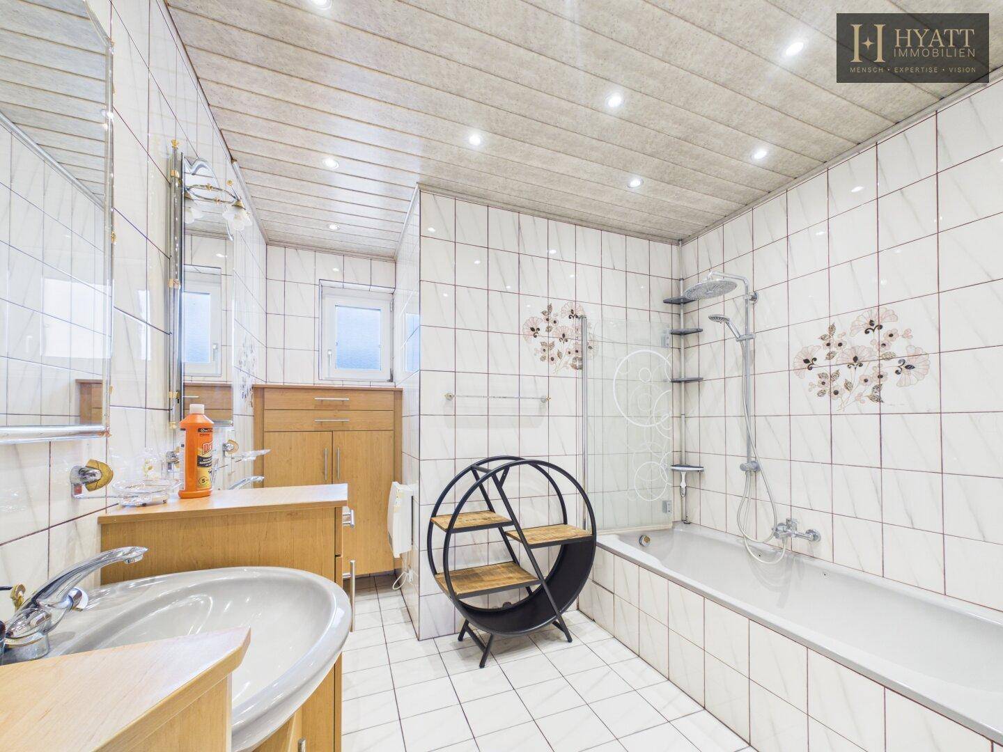 Gefliestes Badezimmer mit Badewanne, Duschfunktion, Waschbecken und Holzdecke.