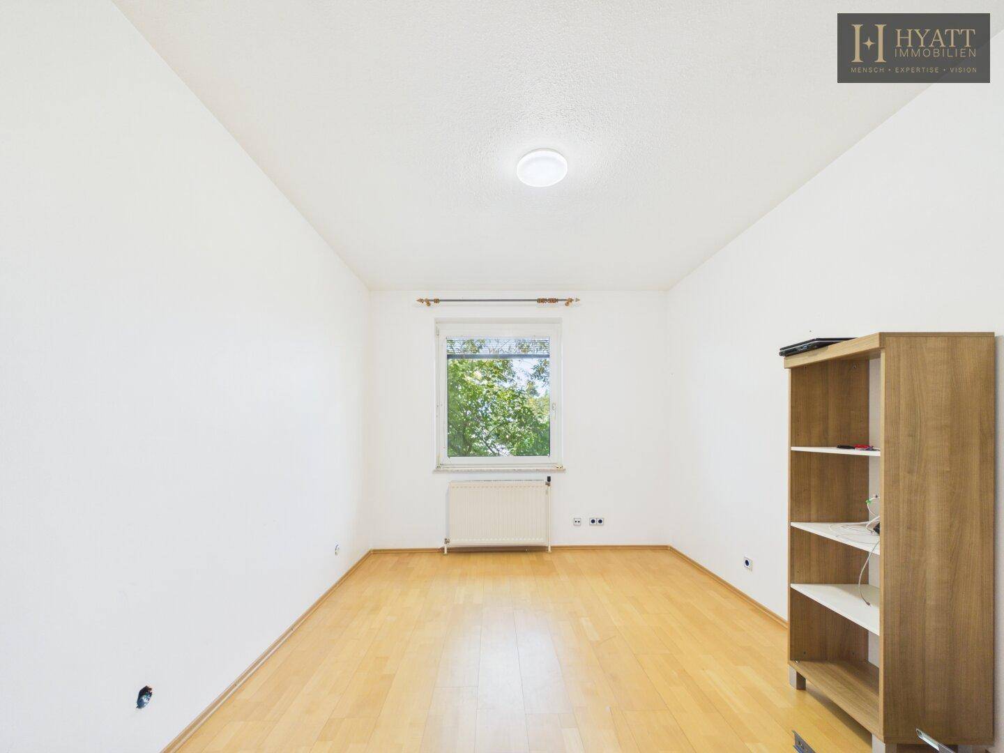 Helles Schlafzimmer mit Holzboden, weißen Wänden und einem Fenster mit Blick ins Grüne.