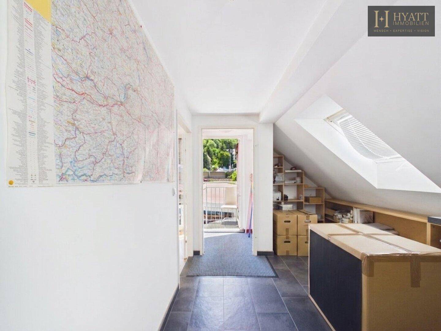 Dachgeschossflur mit Schrägen, einem großen Wandplan und Zugang zu einem kleinen Balkon.