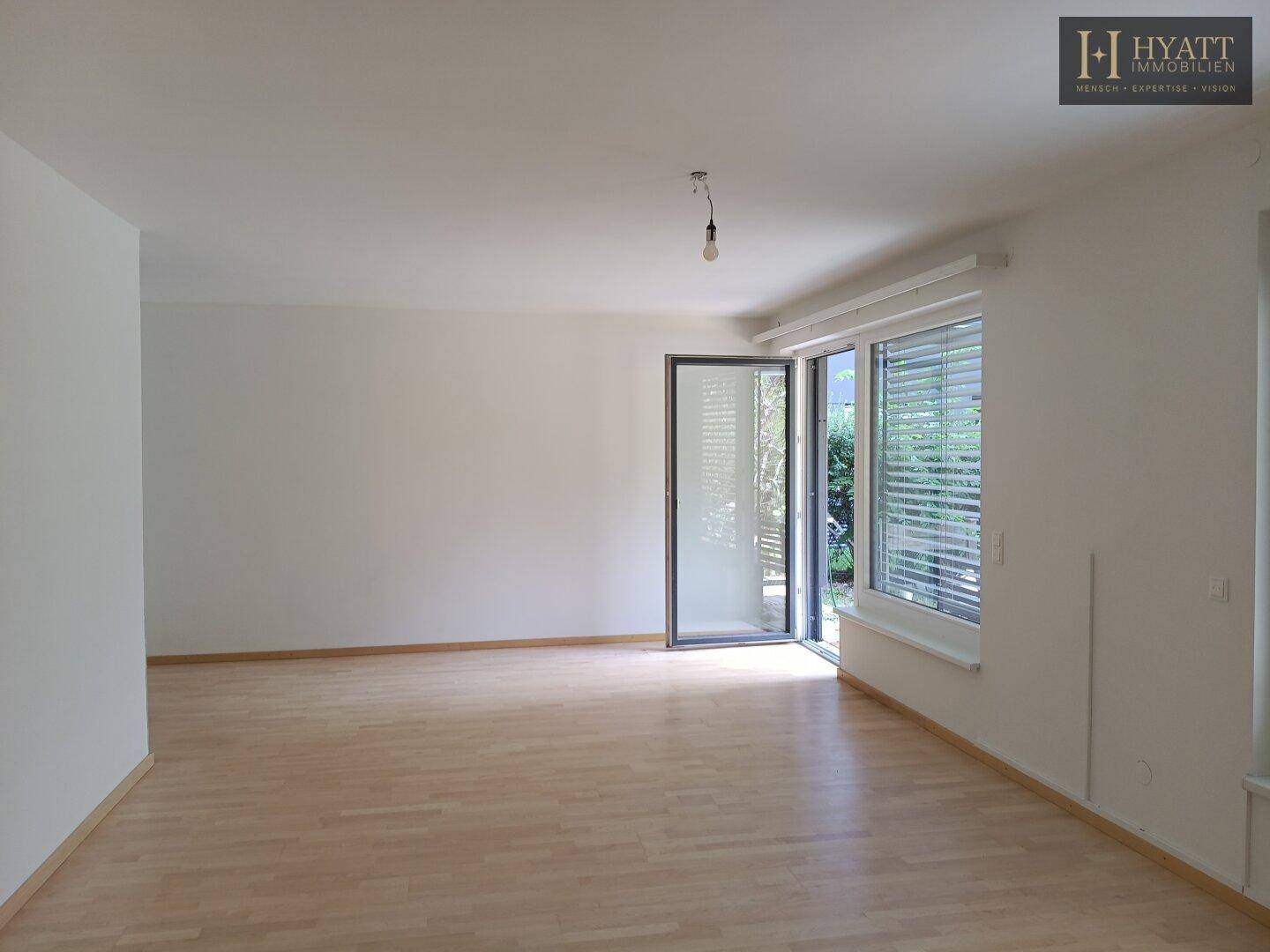 Geräumiger, leerer Wohnbereich mit hellem Holzfußboden und Zugang zu einem Außenbereich.
