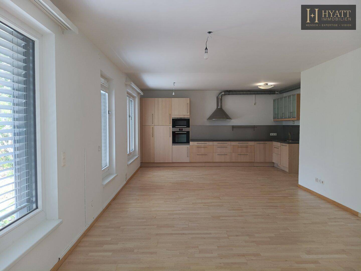Offene Küche mit hellen Holzschränken und integrierten Geräten, angrenzend an einen hellen Wohnbereich.