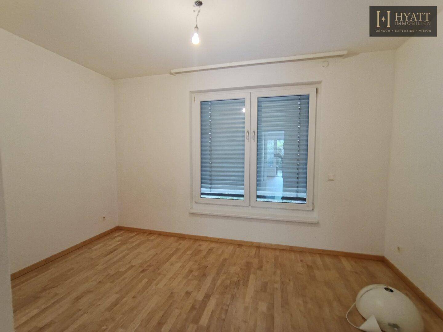 Helles Zimmer mit Holzfußboden und großem Fenster, ideal als Schlaf- oder Arbeitszimmer.