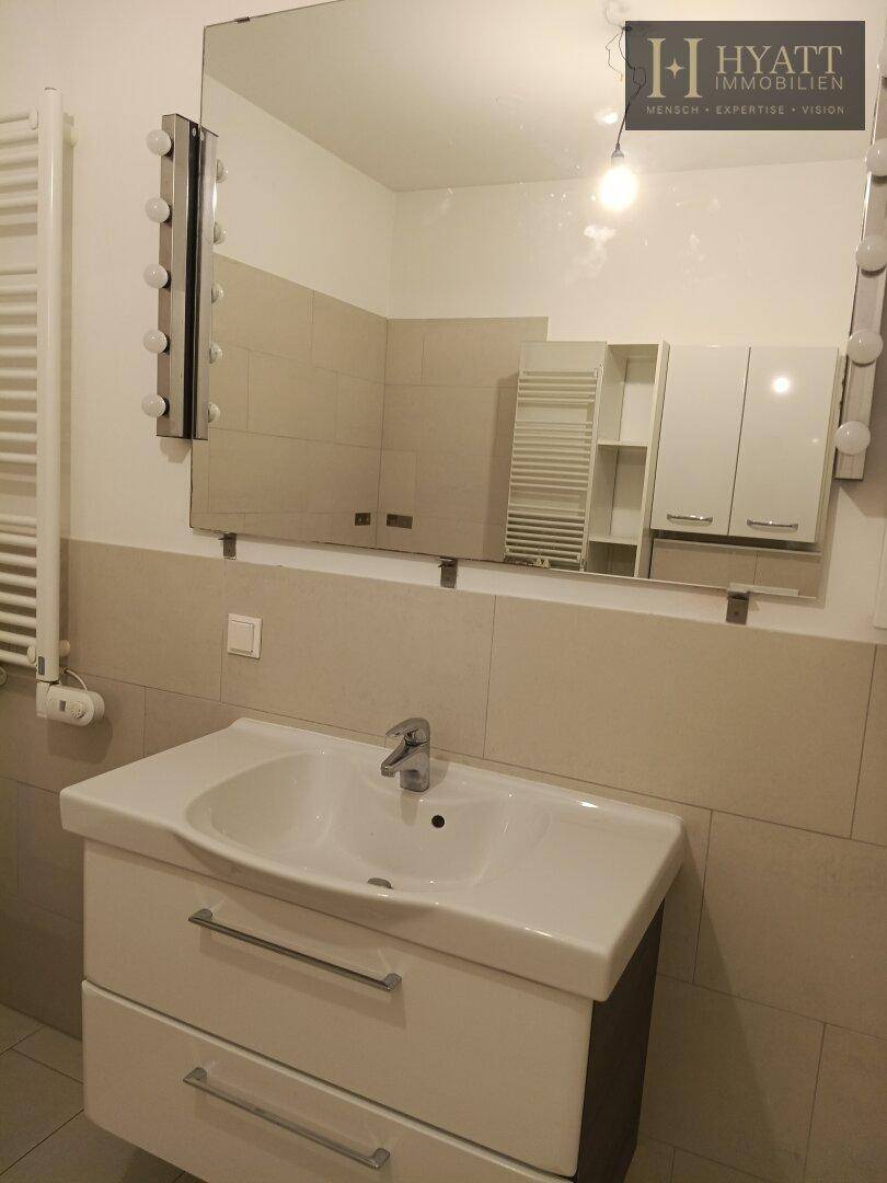 Waschtisch mit Unterschrank und großem Spiegel mit integrierter Beleuchtung im Badezimmer.
