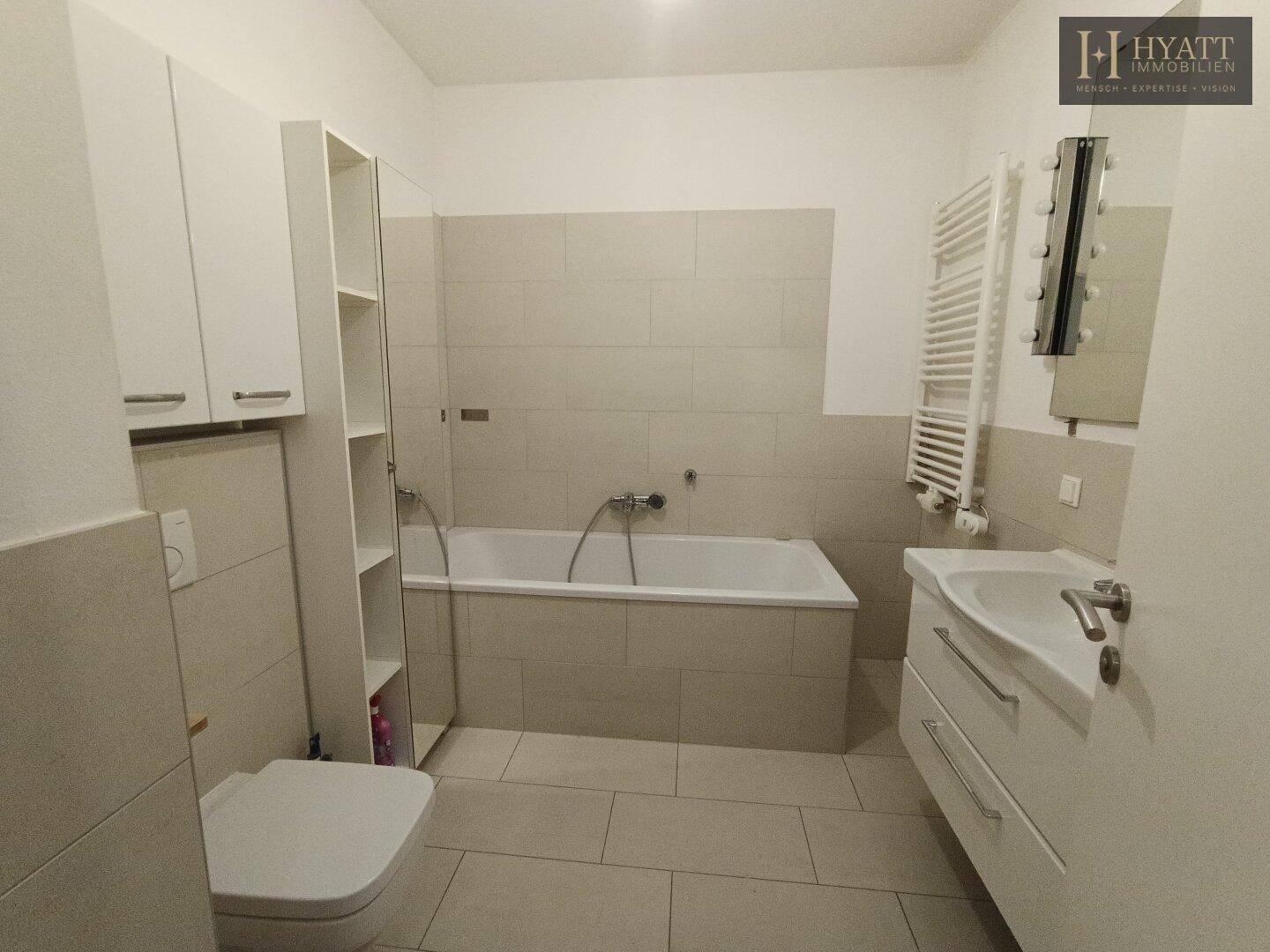 Modernes Badezimmer mit Badewanne, Waschtisch, WC und beheiztem Handtuchhalter.