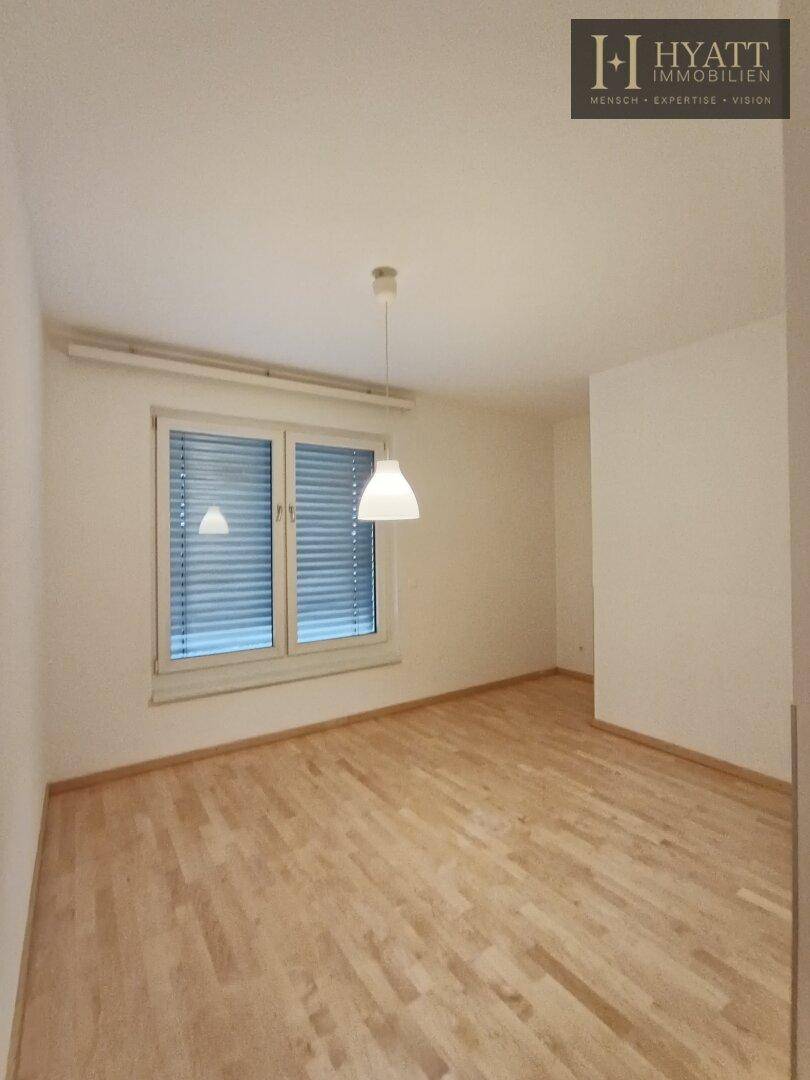 Freundliches Zimmer mit Parkettboden und Fenster, ausgestattet mit einer modernen Pendelleuchte.
