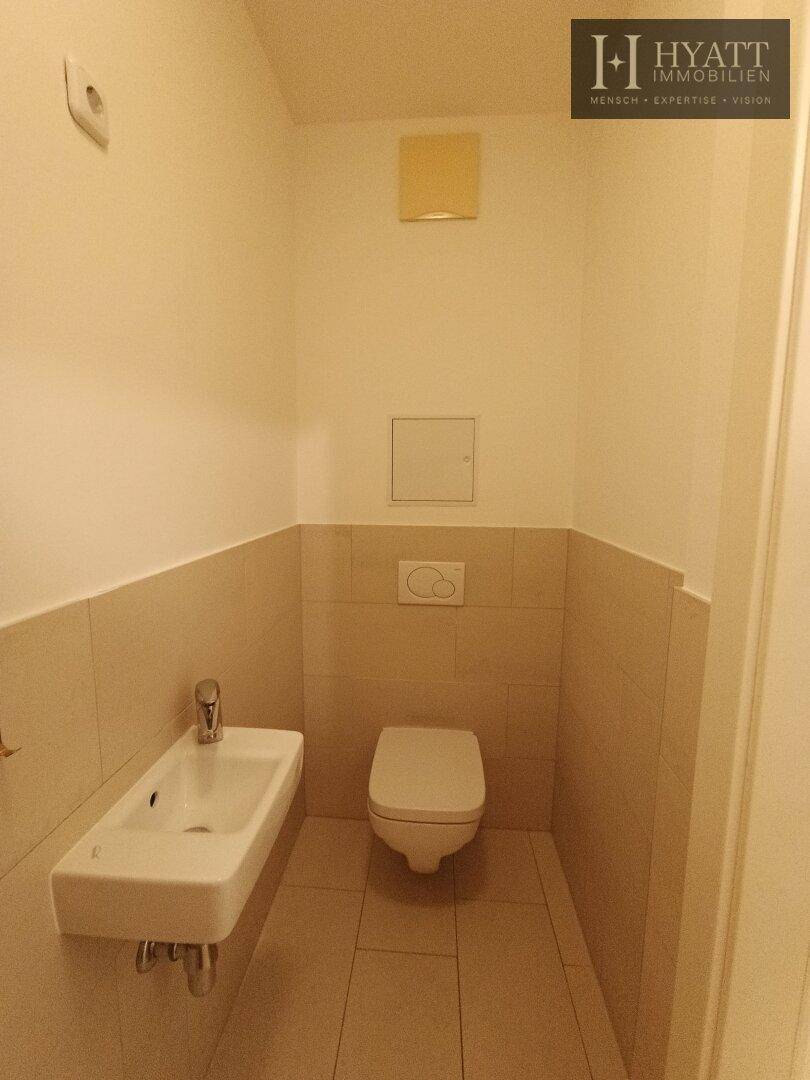 Kleines Gäste-WC mit Wand-WC und Handwaschbecken, in hellen Fliesen gehalten.