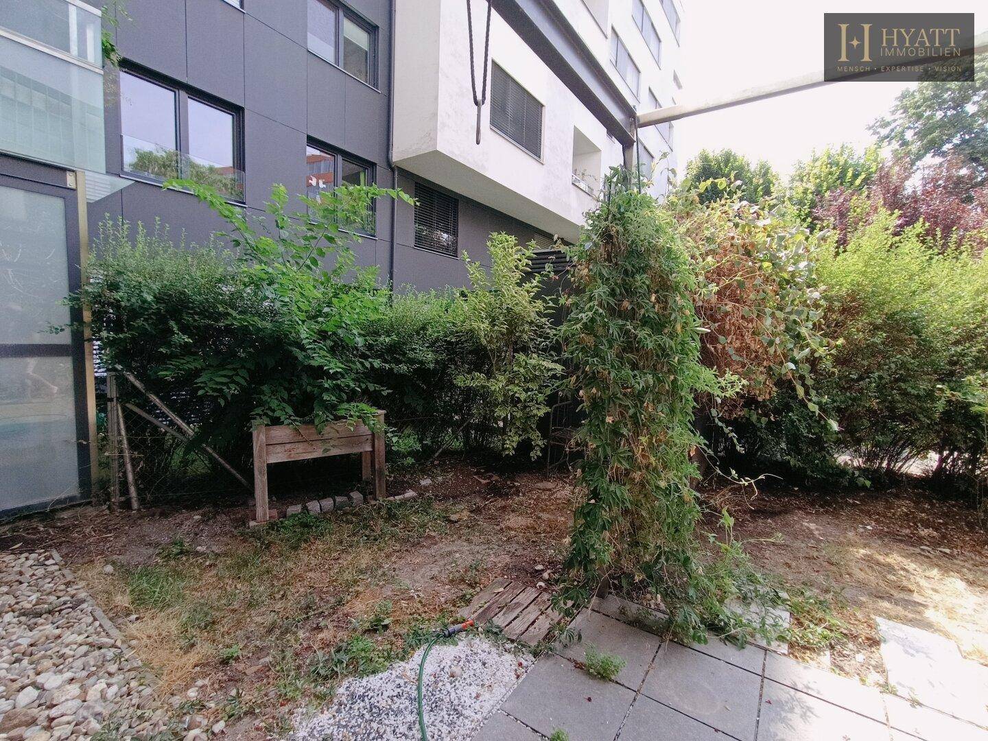Gartenbereich neben dem Gebäude mit Sträuchern und einem erhöhten Pflanzbeet.