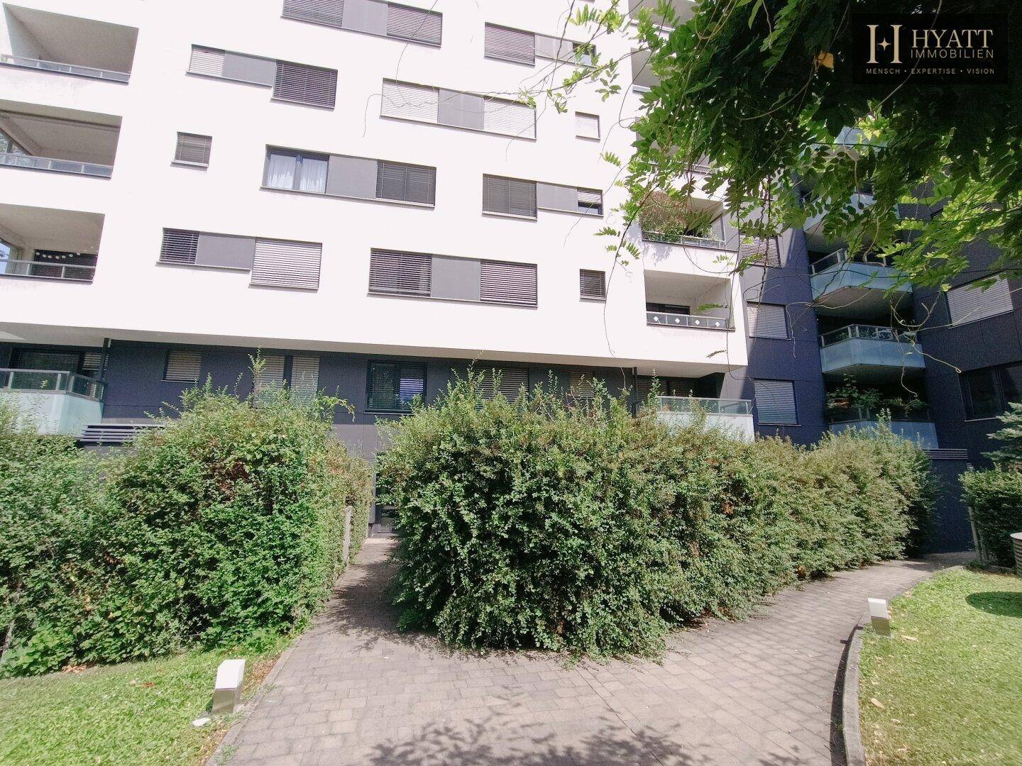Moderne Wohnanlage mit Balkonen und gepflegten Grünflächen, zugänglich über einen Gehweg.