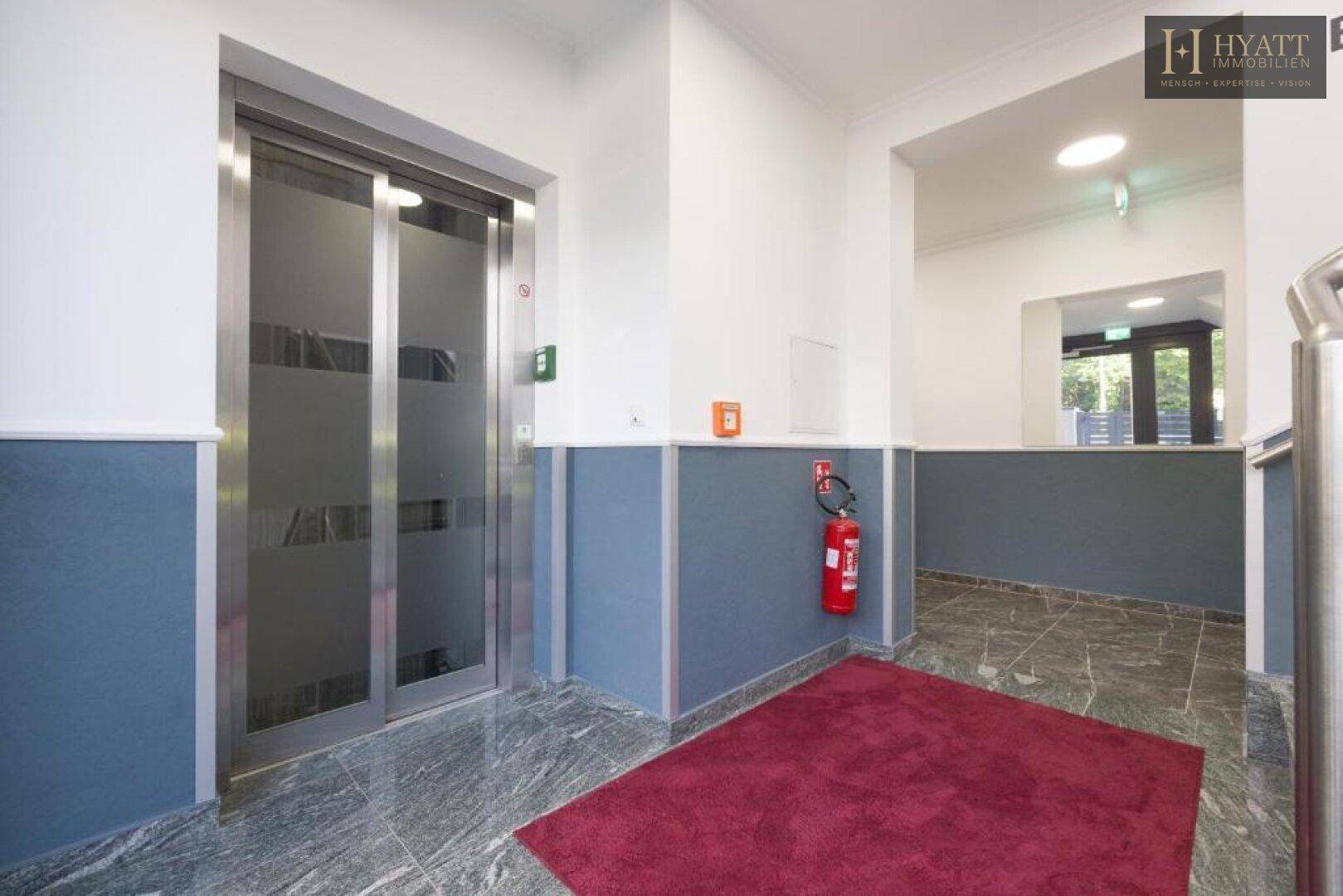 Heller Flur im Gebäude mit modernem Aufzug und gefliestem Boden.