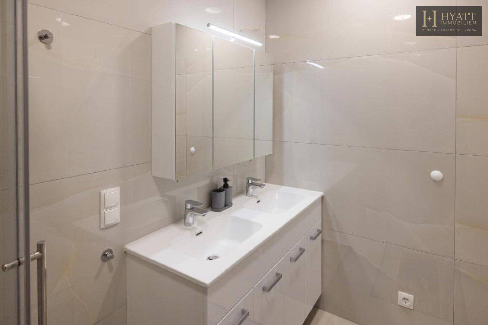 Modernes Badezimmer mit Doppelwaschbecken, Spiegelschrank und großen hellen Fliesen.