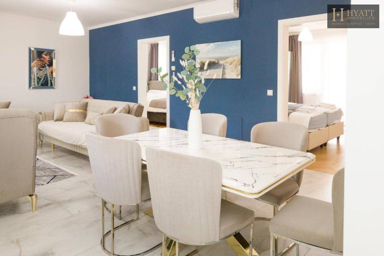Offener Wohn-Essbereich mit elegantem Esstisch, blauer Wand und Zugang zu weiteren Räumen.