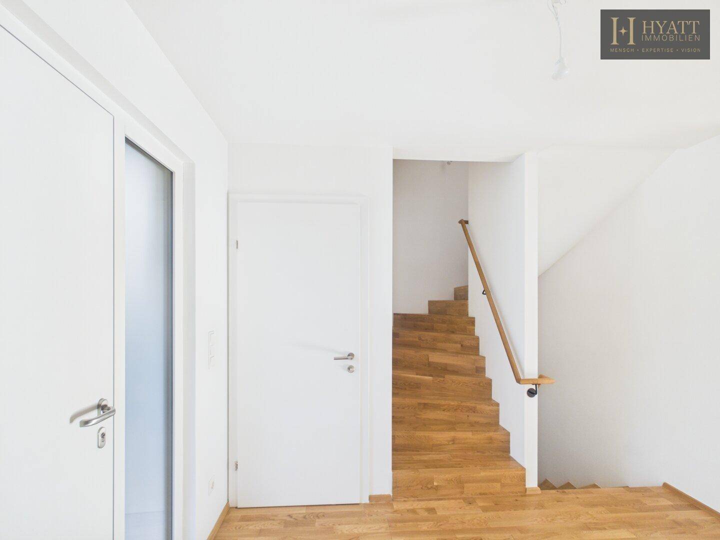 Heller Flur mit Holztreppe und weiß gestrichenen Wänden.