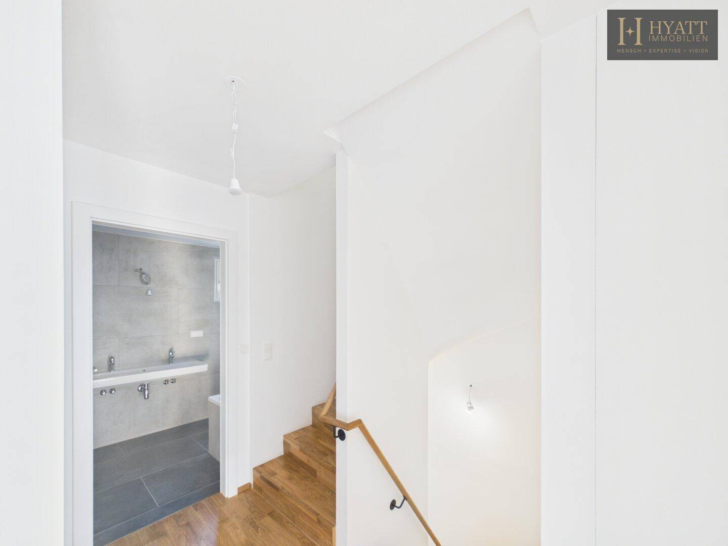 Heller Flur mit Holztreppe und Blick in ein modernes Badezimmer.