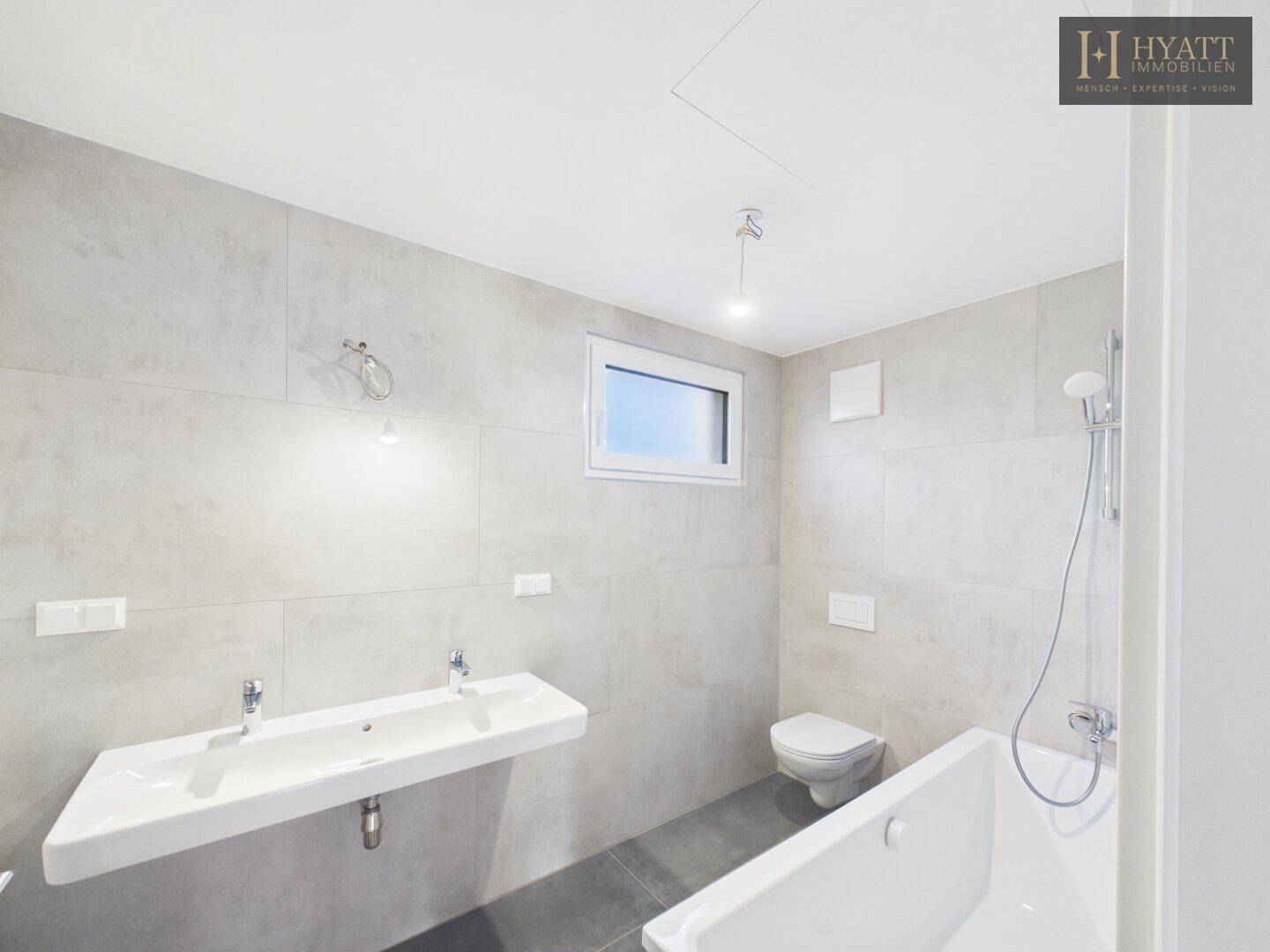 Modernes Badezimmer mit Doppelwaschbecken, Badewanne und hellgrauen Fliesen.