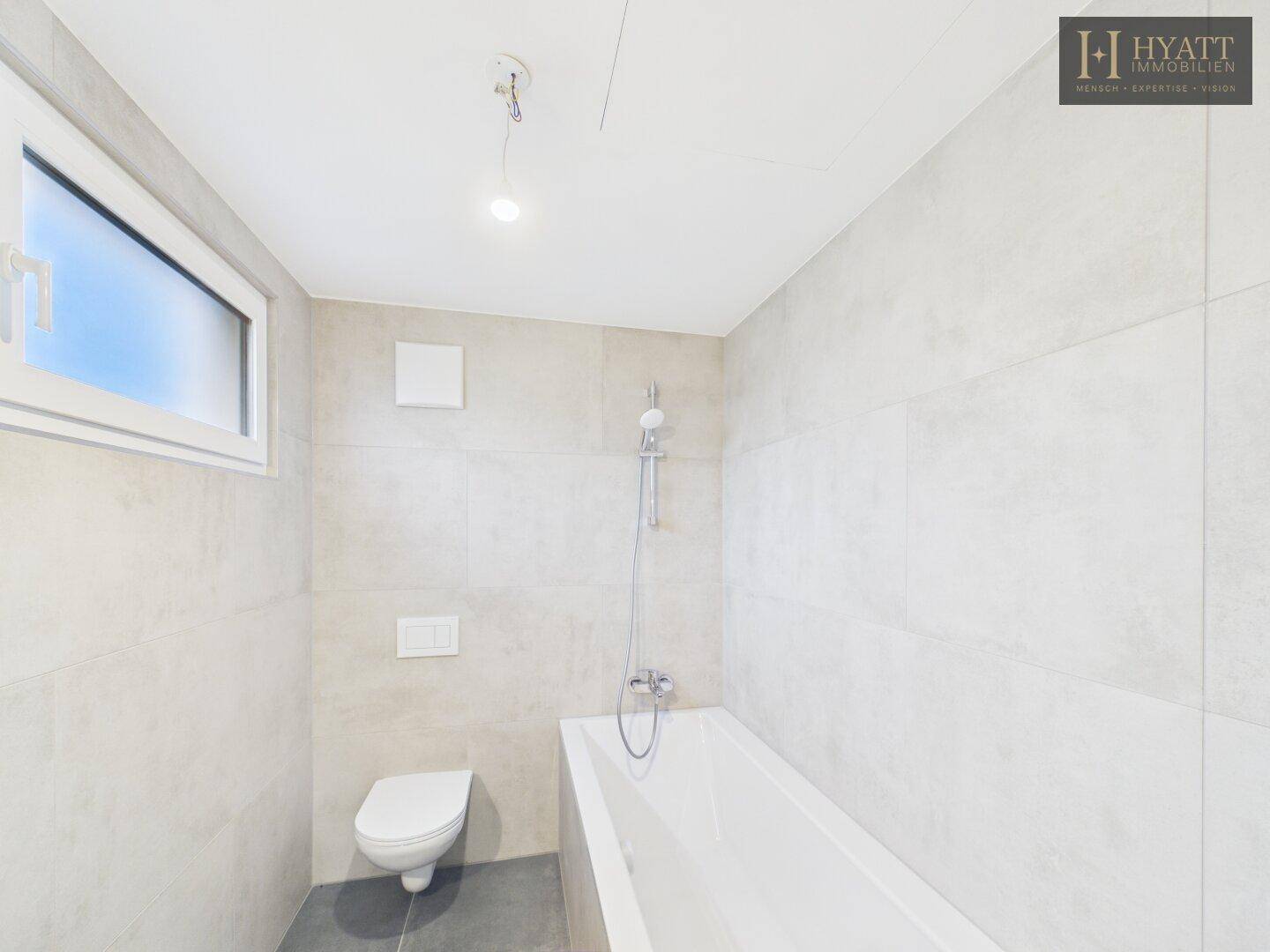Modernes Badezimmer mit Badewanne, WC und hellgrauen Fliesen.