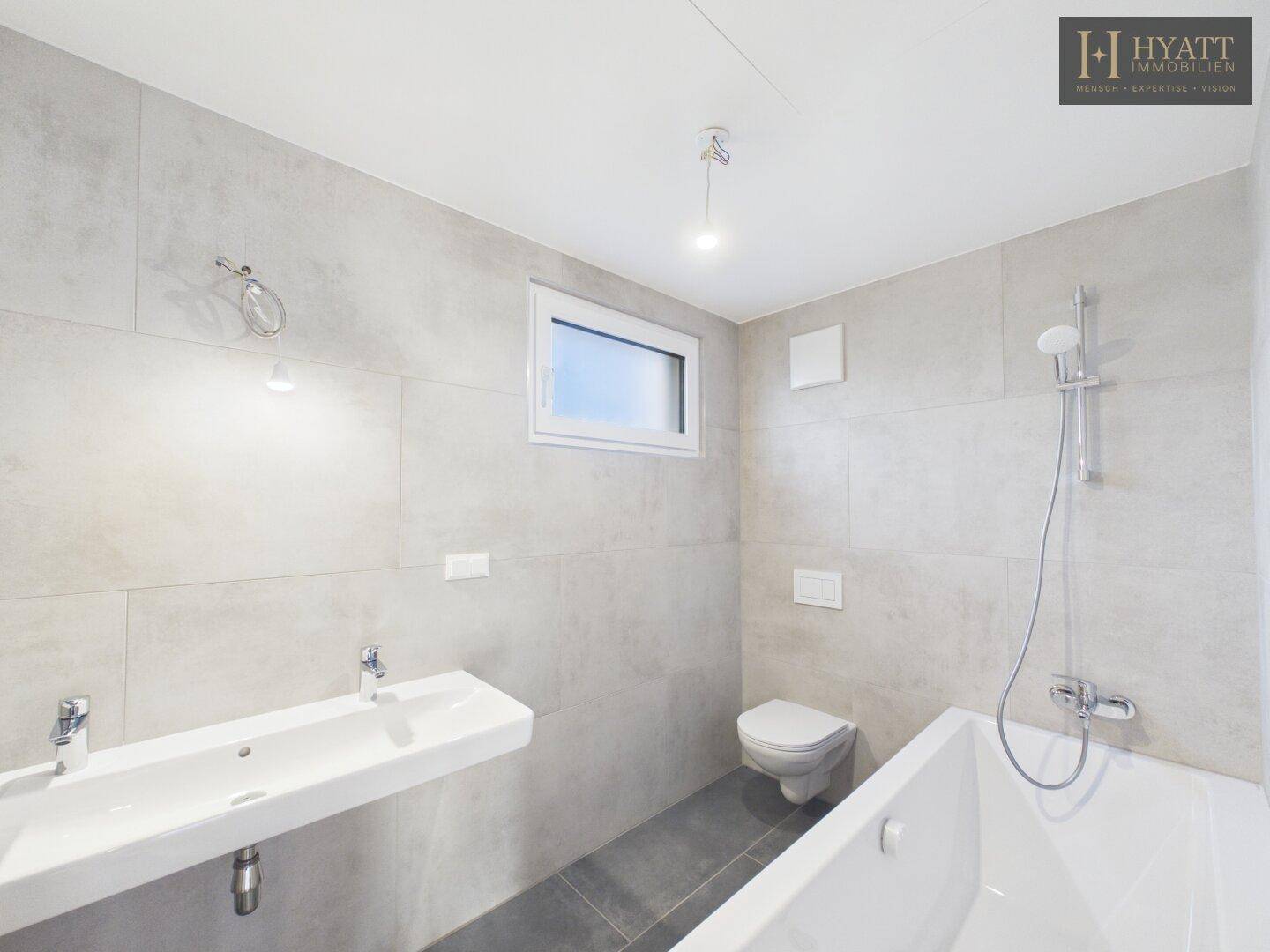 Modernes Badezimmer mit Doppelwaschbecken, Badewanne und hellgrauen Fliesen.