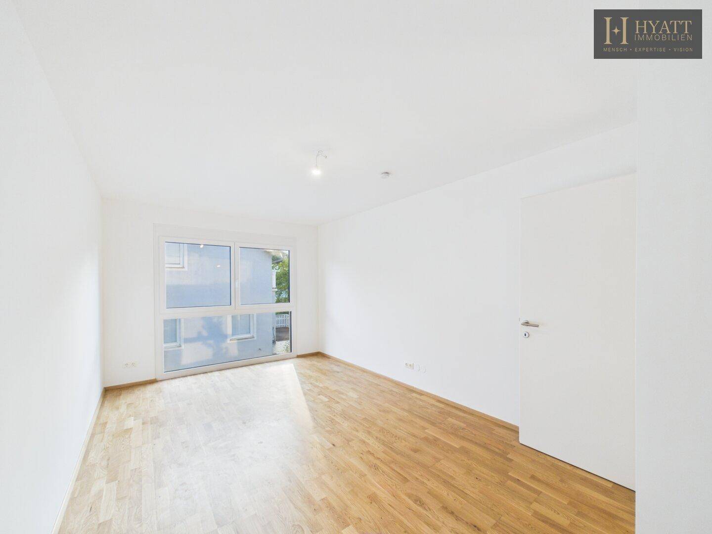 Helles Schlafzimmer mit Parkettboden und großem Fenster für viel Tageslicht.