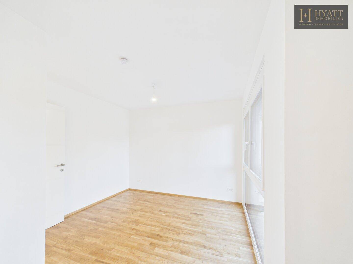 Geräumiges Schlafzimmer mit Holzboden und Fenster, bereit zur individuellen Gestaltung.