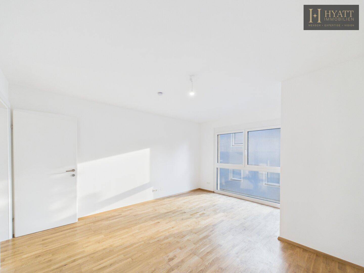 Helles Schlafzimmer mit Holzboden und großem Fenster, ideal für Ruhe und Erholung.