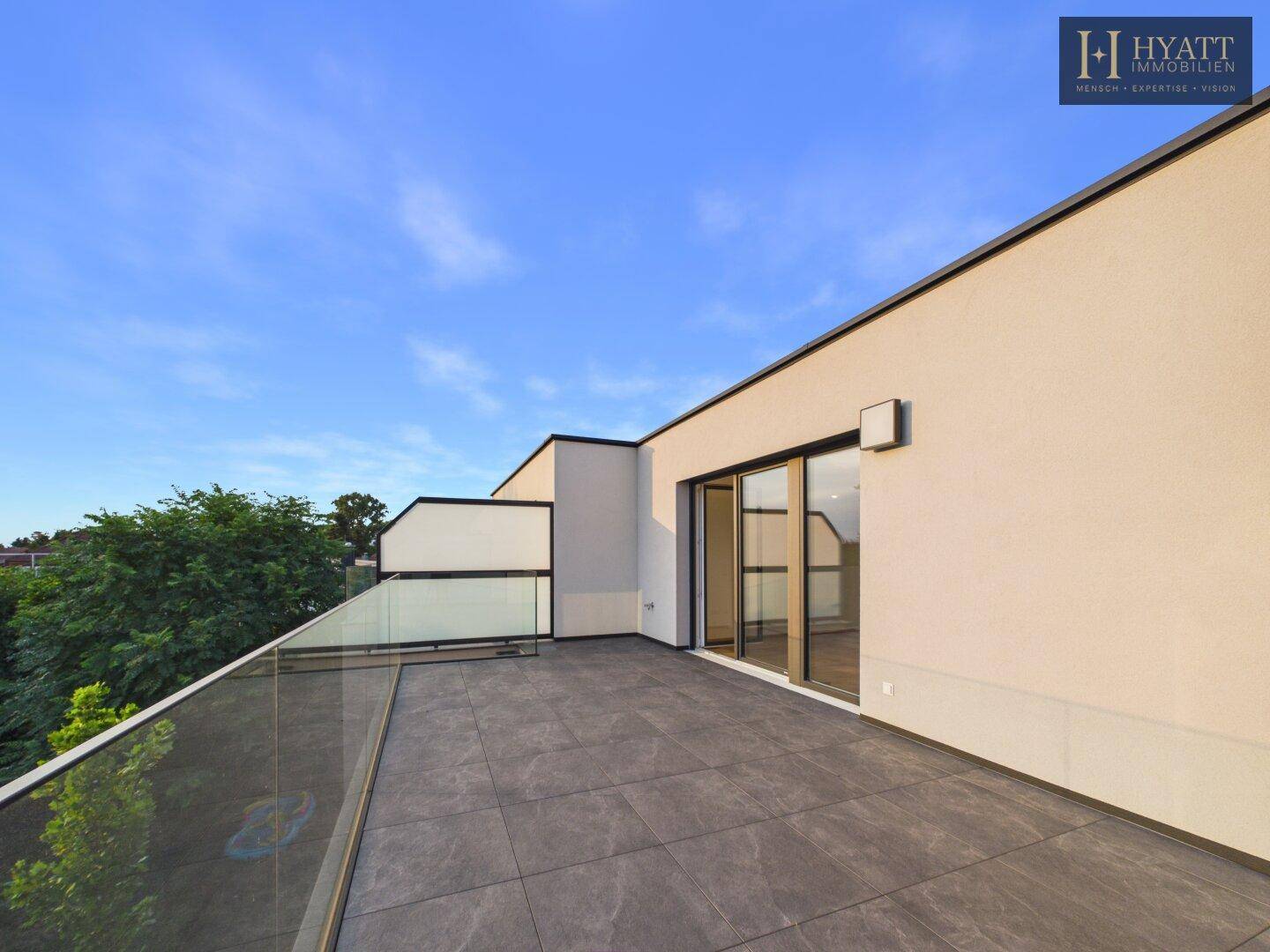 Geräumige Dachterrasse mit modernen Fliesen, Glasgeländer und weitem Ausblick.