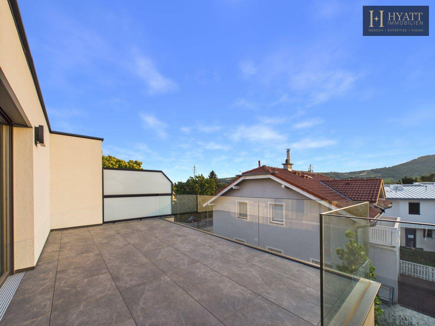 Weitläufige Dachterrasse mit moderner Fliesenoptik und Panoramablick auf die Umgebung.
