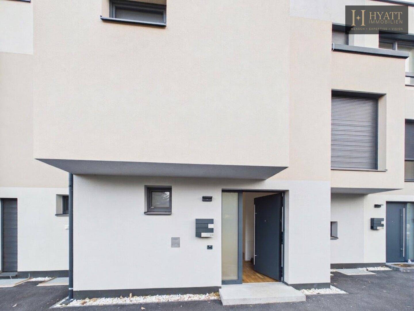 Eingangsbereich eines modernen Hauses mit dunkler Tür und weißer Fassade.