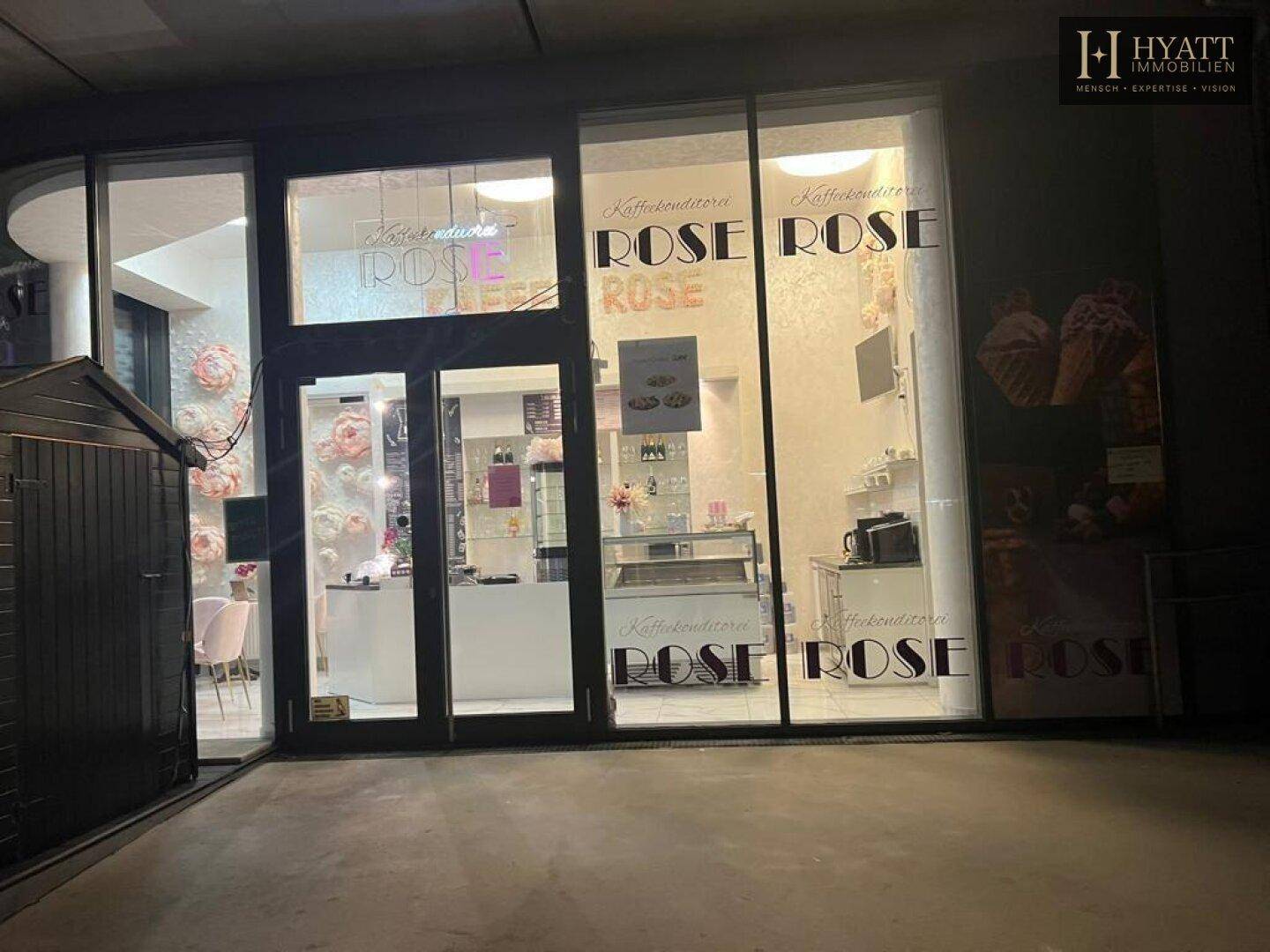Fassade eines Cafés bei Nacht mit großen Schaufenstern und beleuchtetem Innenbereich.