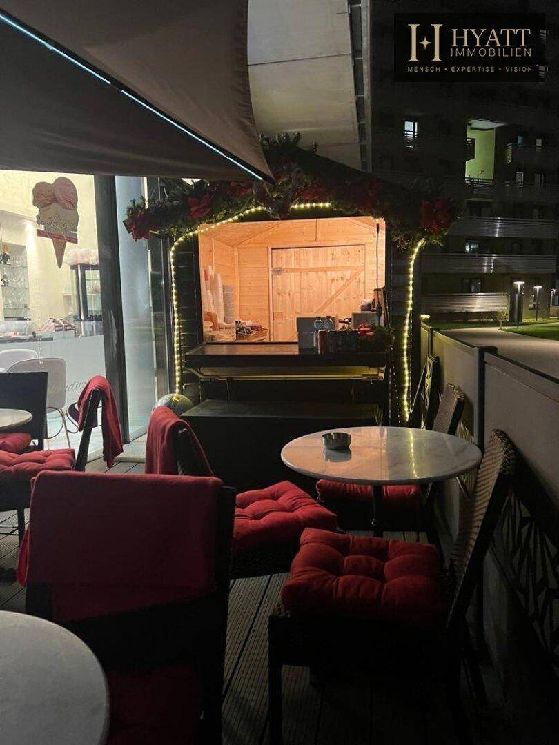 Außenbereich eines Cafés bei Nacht mit festlicher Dekoration, Tischen und einer kleinen Holzhütte.
