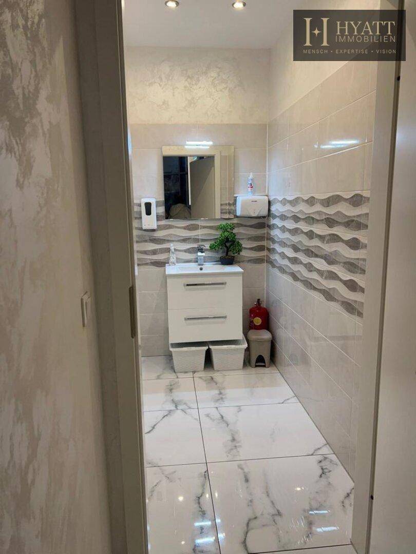 Modernes Badezimmer mit weißem Waschtisch, Spiegel und hellen Fliesen an Wänden und Boden.