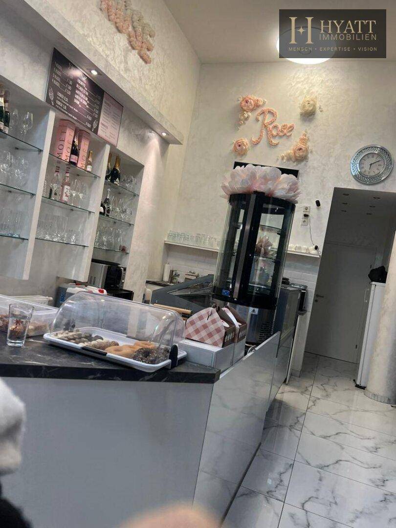 Thekenbereich eines Cafés mit Gebäckvitrine, Regalen und dekorativen Elementen an der Wand.