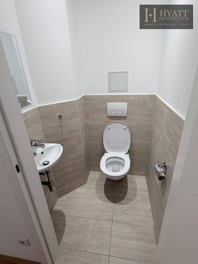 Modernes Gäste-WC mit beigefarbenen Fliesen, wandhängendem WC und kleinem Waschbecken.