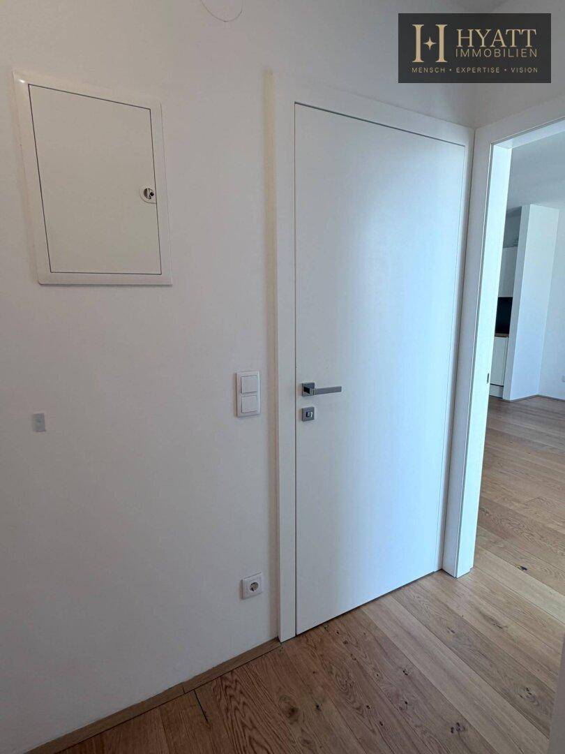 Heller Flur mit Holzboden und weißer Tür, die zu weiteren Räumen der Wohnung führt.