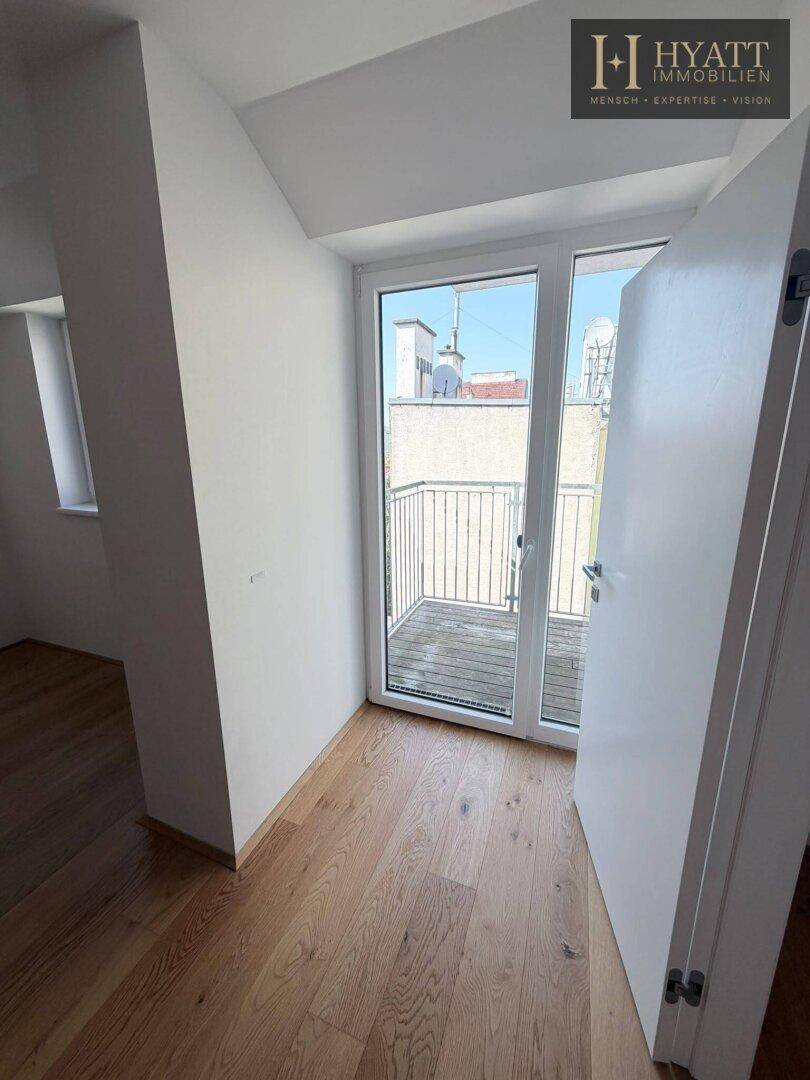 Heller Raum mit Holzboden und großen Fenstern, die den Zugang zu einem kleinen Balkon bieten.