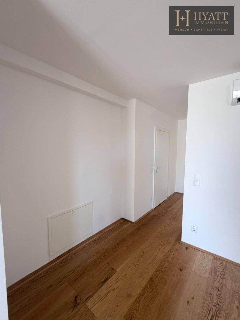 Geräumiger Flur mit Holzboden und weiß gestrichenen Wänden, der zu anderen Bereichen führt.