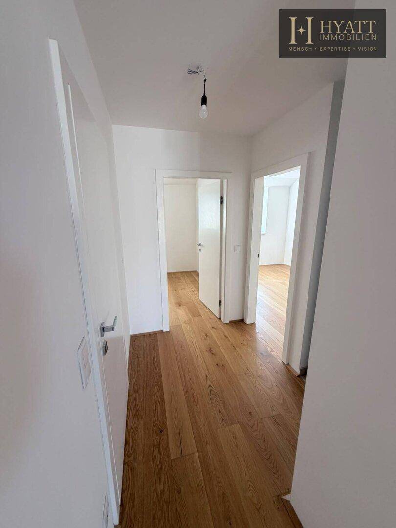 Langer, heller Flur mit Holzboden, der den Zugang zu mehreren Zimmern ermöglicht.