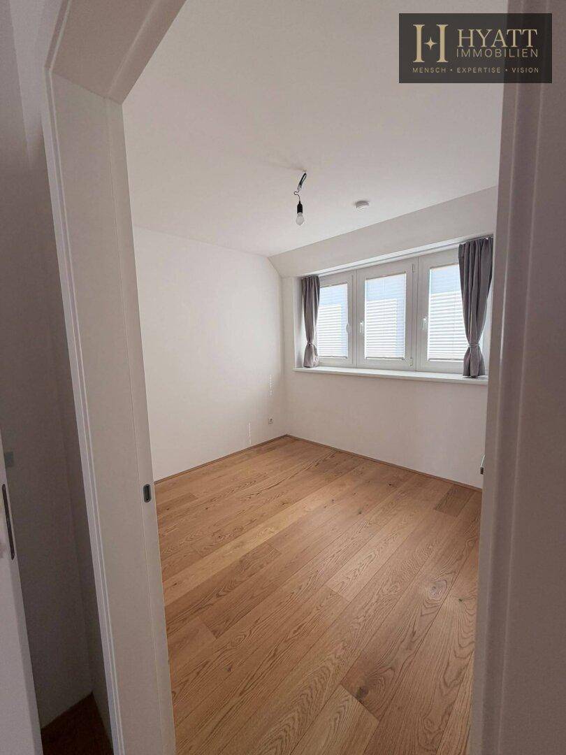 Helles Schlafzimmer mit Holzboden und großen Fenstern, die viel Tageslicht hereinlassen.