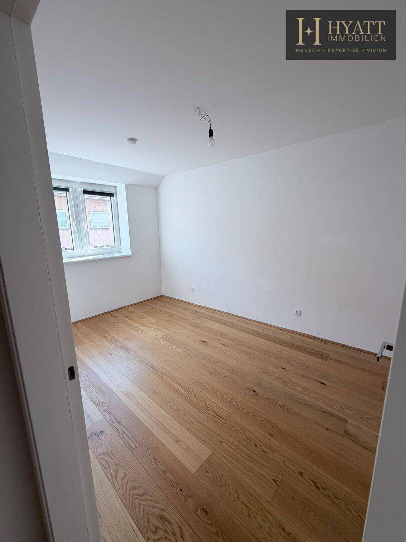 Geräumiges Schlafzimmer mit Holzboden und weißen Wänden, bereit zur individuellen Gestaltung.